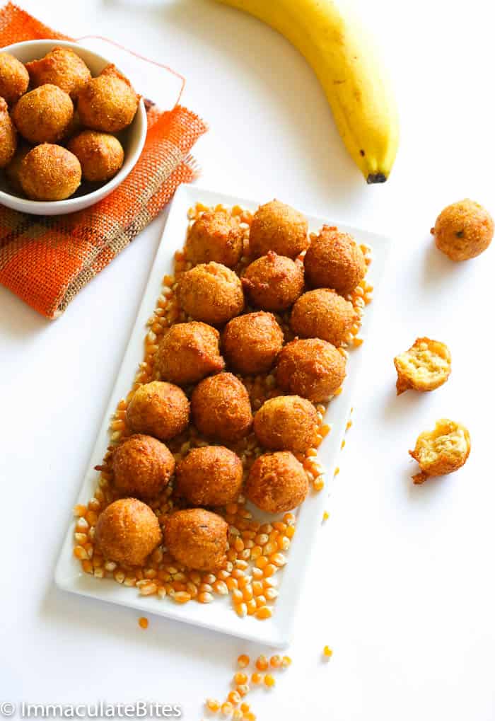 A plateful of Accra banana with a fresh banana in the background. A delicious banana fritter treat 