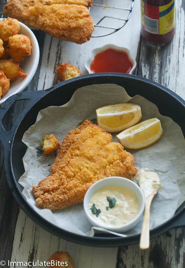 Comfort food Southern Fried Catfish on a black plate with homemade tartar sauce and lemon wedges