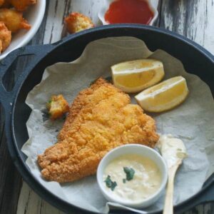 Comfort food Southern Fried Catfish on a black plate with homemade tartar sauce and lemon wedges