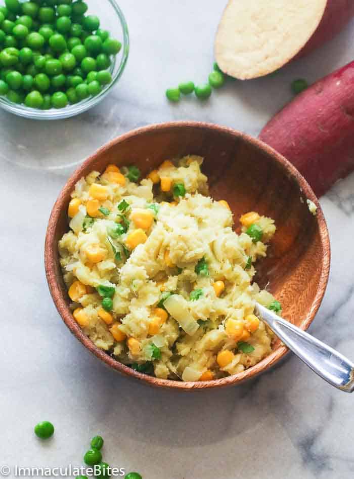 a wooden bowl of irio with some peas in the background