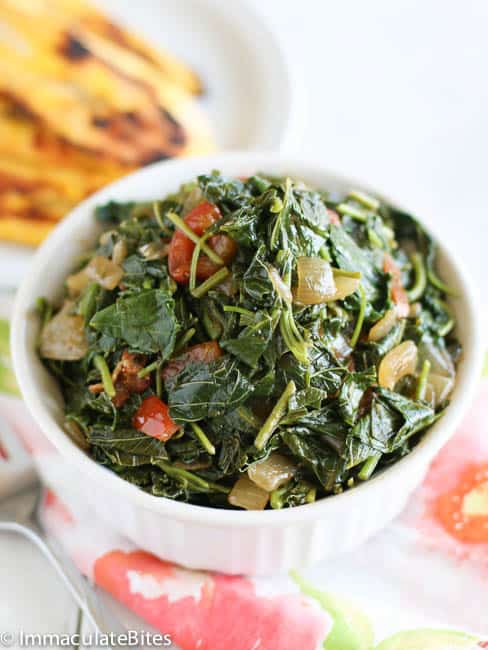 A bowl of callaloo in a white bowl and fried sweet plantains in the background