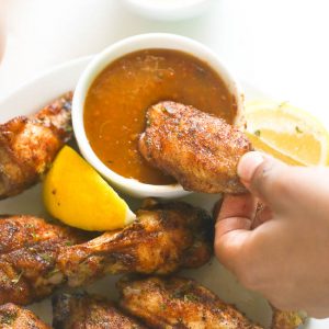 Dipping baked jerk chicken wings in a delectable hot sauce