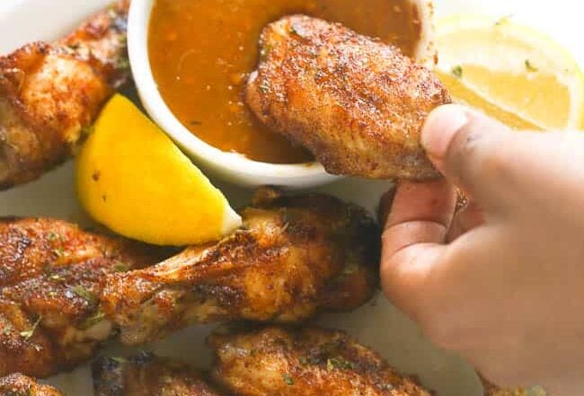 Dipping baked jerk chicken wings in a delectable hot sauce