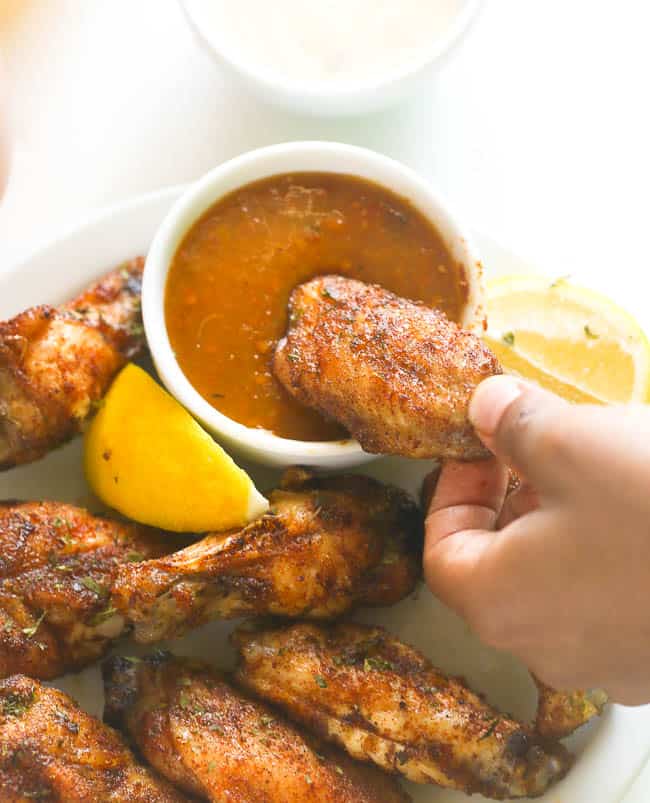 Dipping baked jerk chicken wings in a delectable hot sauce