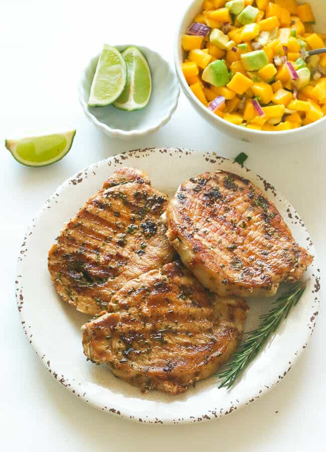 Three Marinated Rosemary Pork Chops Served with Lime Wedges and Mango Salsa