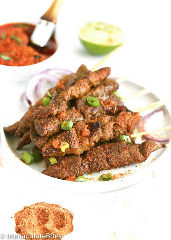 A Plate of Curry Beef Satay in Skewers with Sauce in the Background