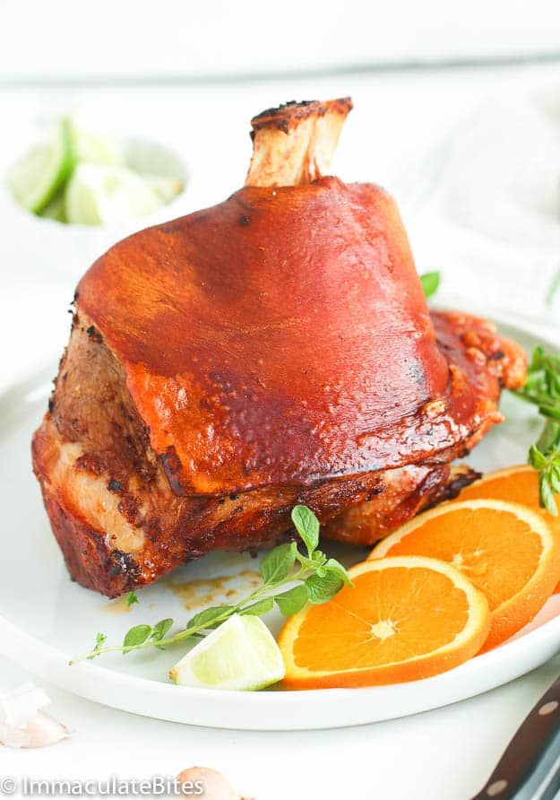 Puerto Rican style pernil on a white platter with orange slices