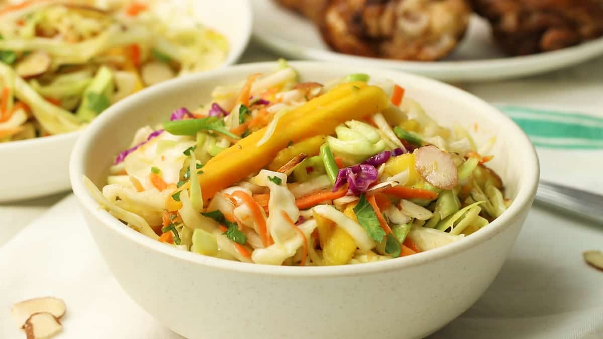 Two Bowls of Caribbean Coleslaw with Chicken in the Background