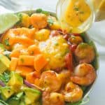 Pouring mango dressing over a mango avocado shrimp salad