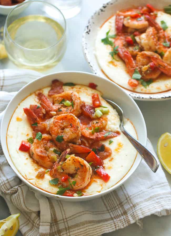 two bowls of creamy Cajun shrimp and grits with a glass of wine in the background