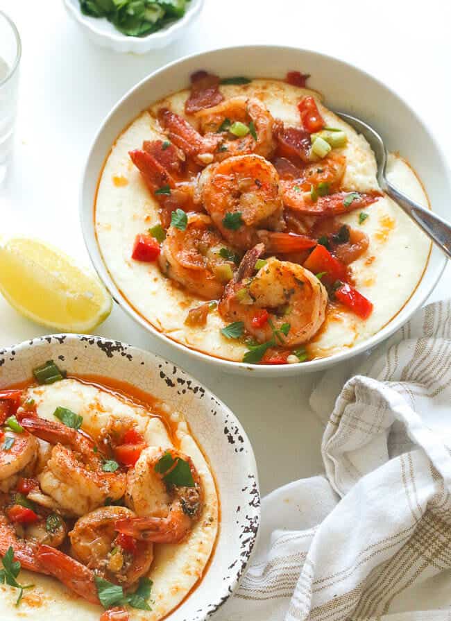 two bowls of creamy Cajun shrimp and grits with a lemon wedge in the background