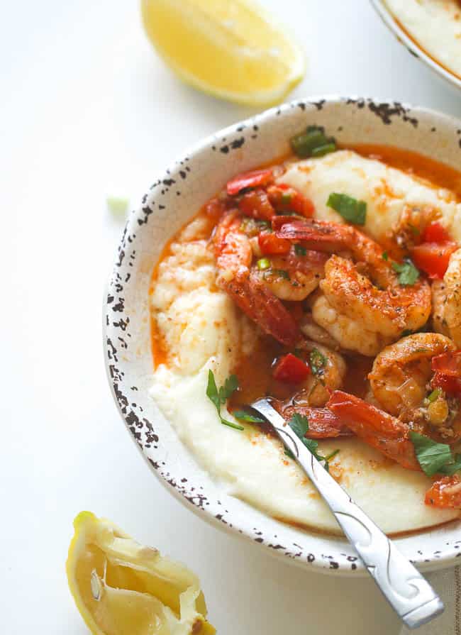 Creamy Cajun Shrimp and Grits being spooned with lemon wedges in the background