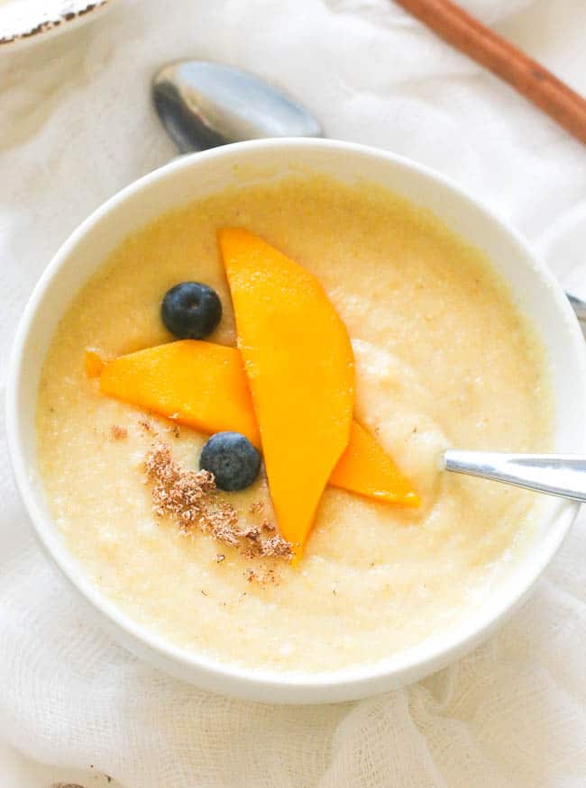 Jamaican Cornmeal Porridge topped with grated nutmeg, mango, and blueberries