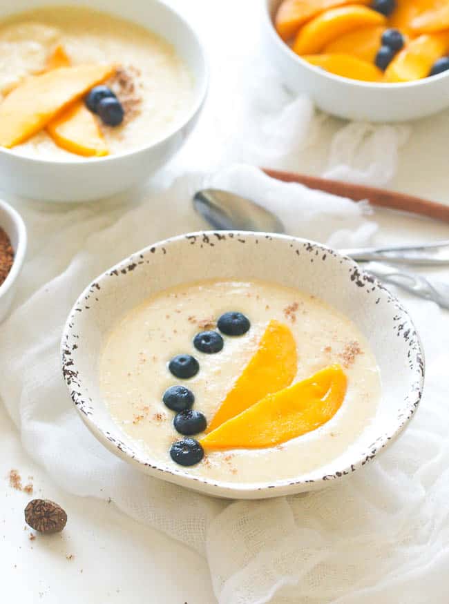 Two bowls of Jamaican cornmeal porridge decorated with blueberries and mango slices