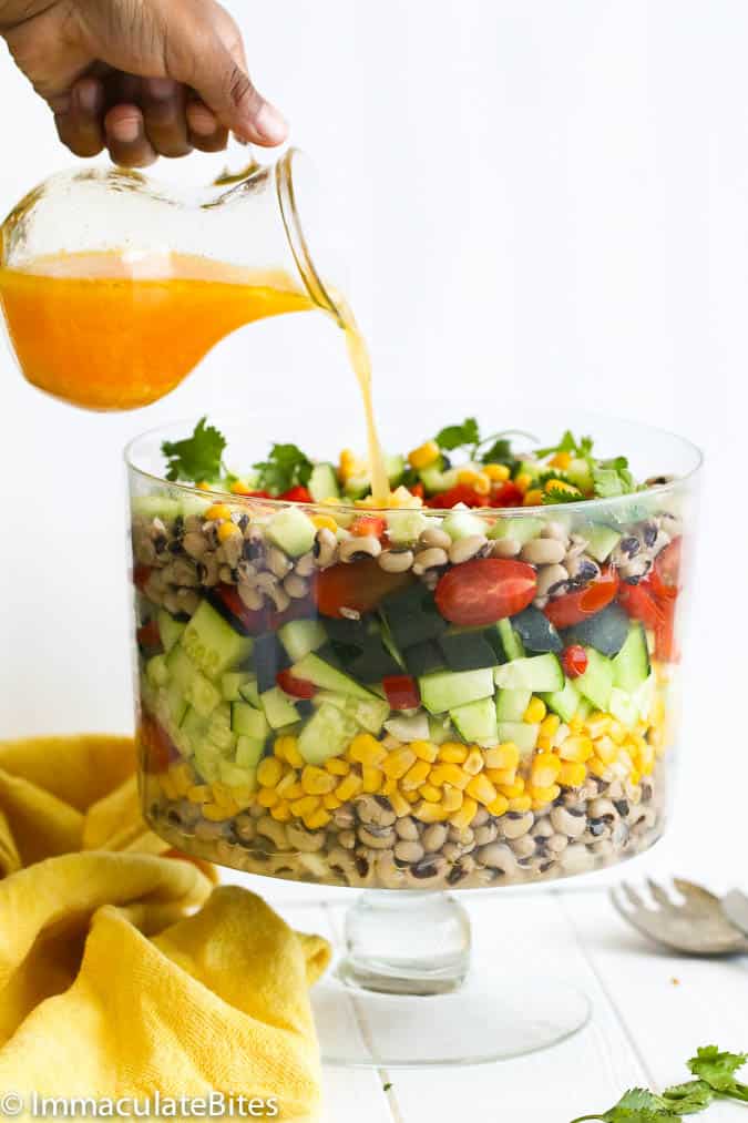 Pouring citrusy dressing over the Black-eyed peas salad in a fancy bowl