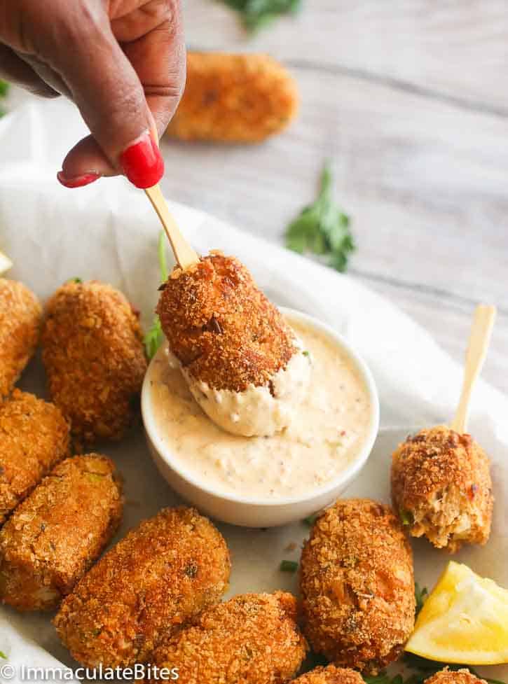 a hand dipping a salmon croquette on stick in remoulade sauce