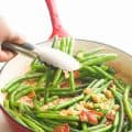 Green Beans with Bacon in a red skillet being served with tongs