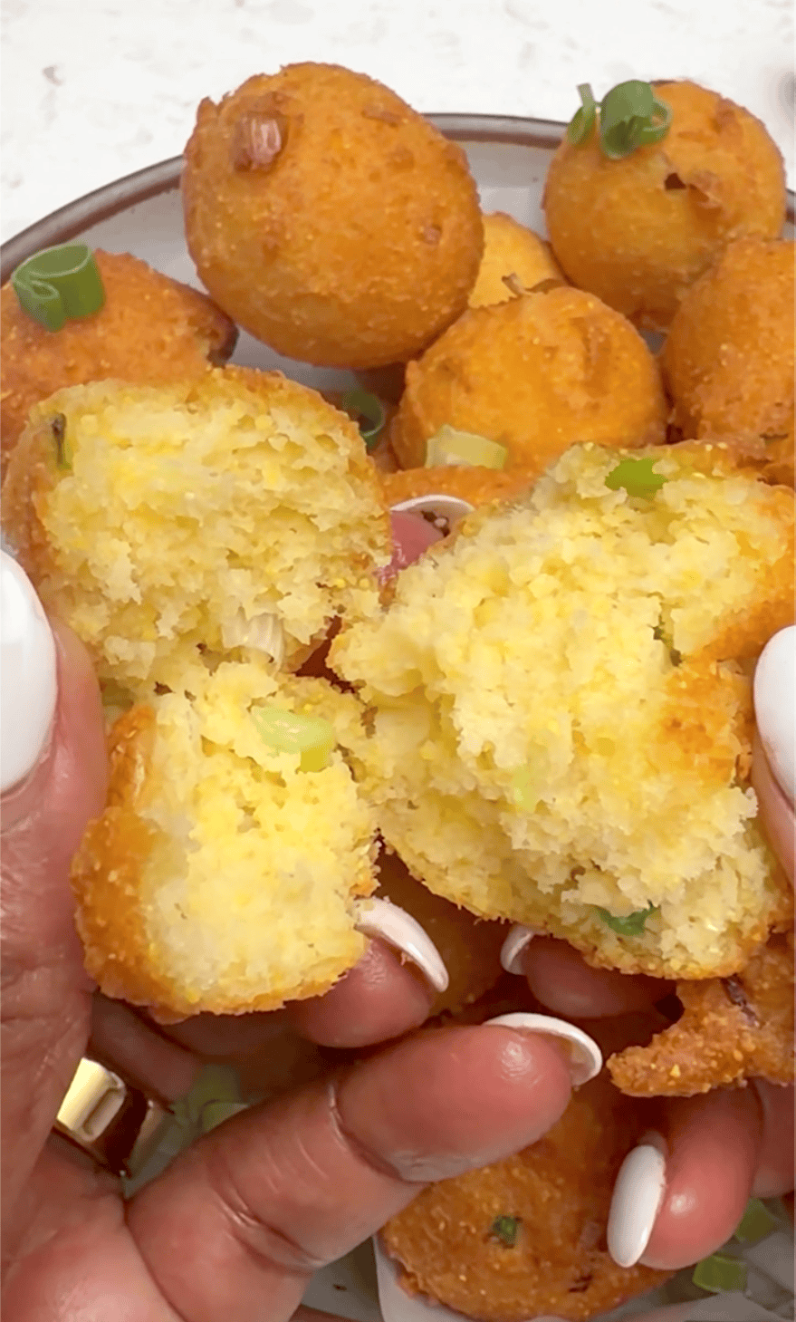 Breaking into a freshly fried hush puppy, exposing the tender middle surrounded by a crispy exterior.
