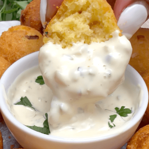 Dipping warm hush puppies into a decadent sauce. Remoulade and ketchup are ideal.