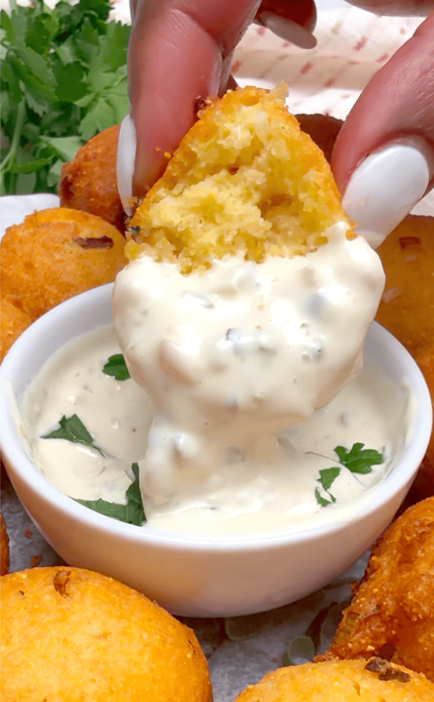 Dipping warm hush puppies into a decadent sauce. Remoulade and ketchup are ideal.