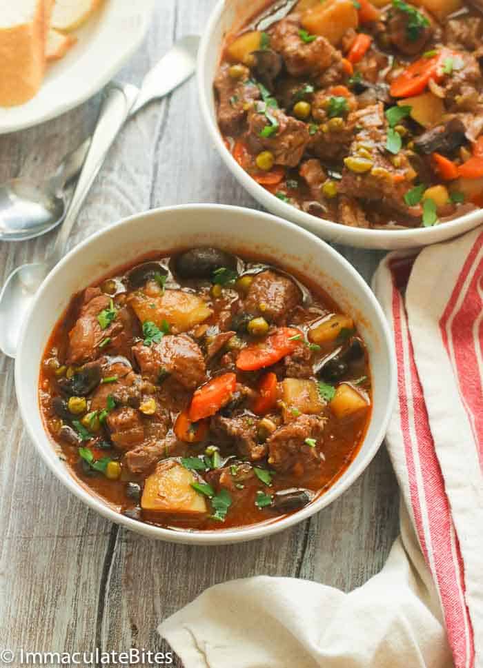 Two bowls of steaming slow cooker beef stew with homemade garlic bread on the side