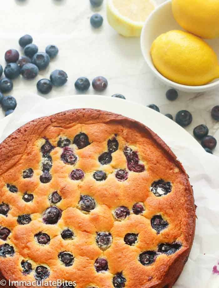 Whole Shot of Blueberry Lemon Cake with Blueberries and Lemon in the Background