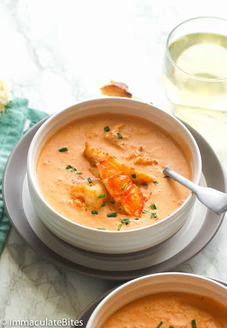 a white bowl of lobster bisque with a dipped spoon and another bowl of bisque in the background