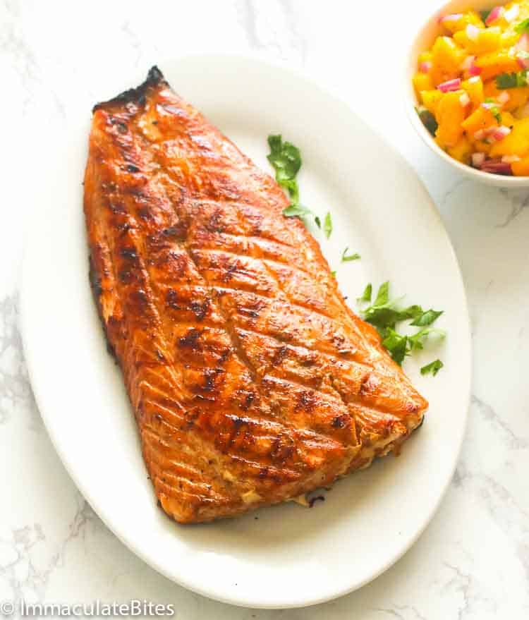 Grilled salmon on a white plate with mango salsa next to it