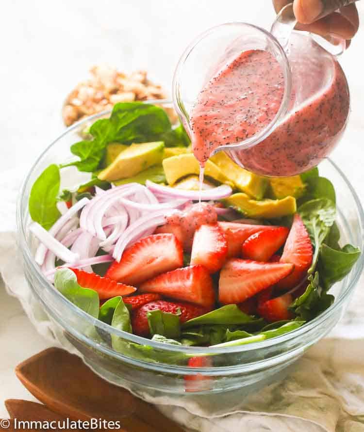 Pouring strawberry poppy salad dressing on a bed of fresh produce
