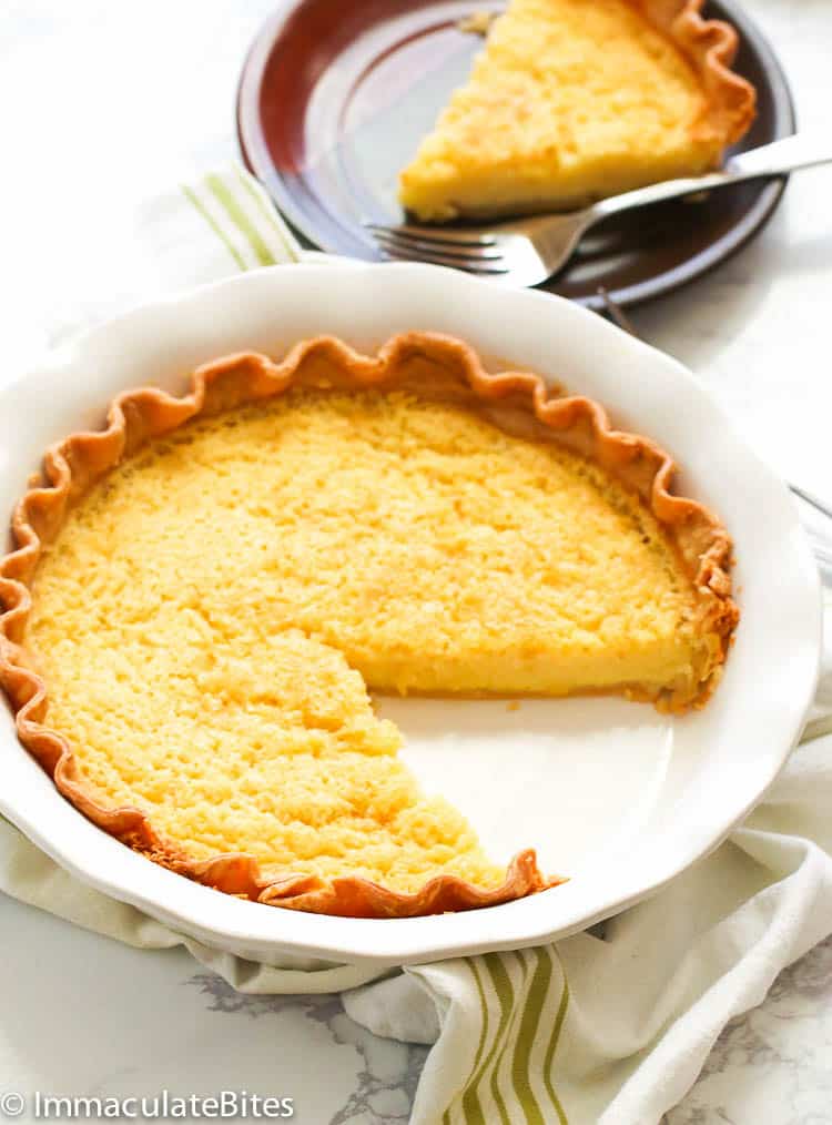 Buttermilk pie in a white pie dish with a slice already served