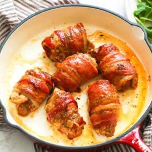Bacon-wrapped chicken in a white skillet with a side salad in the background
