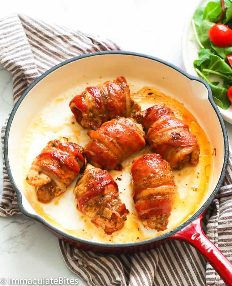 Bacon-wrapped chicken in a white skillet with a side salad in the background