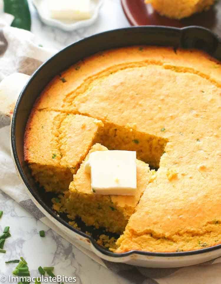 a skillet of cornbread with a slice topped with butter