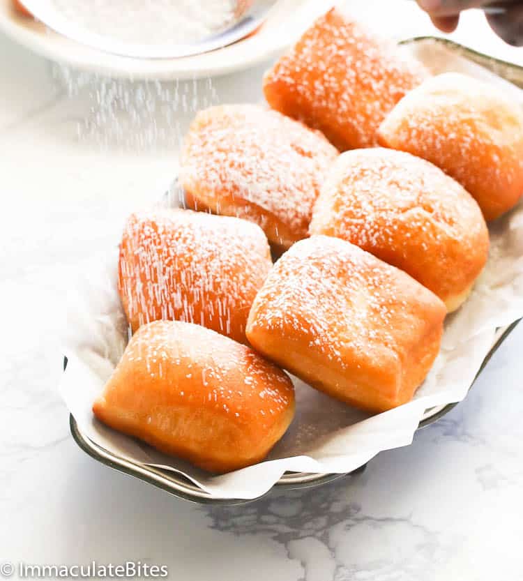 Dusting New Orleans beignets with powdered sugar for a list of foods that start with N.