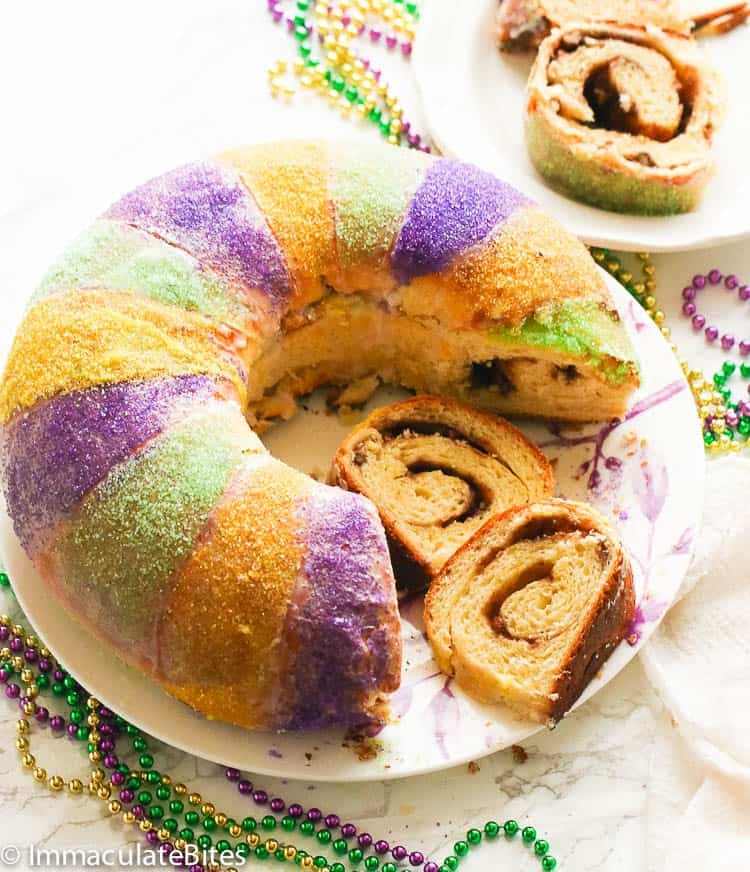 a plate of sliced whole king cake with another plate on the background with two slices of king cake