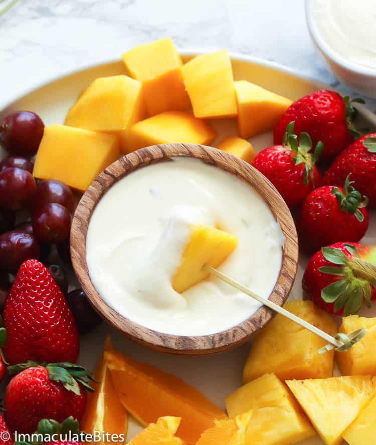 Dipping a pineapple chunk into insanely delicious cream cheese fruit dip