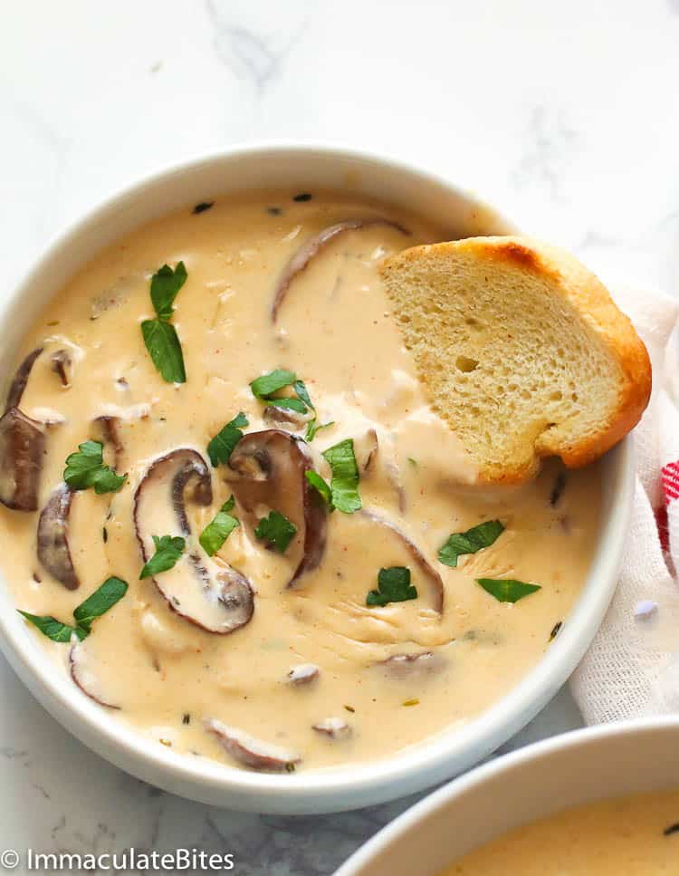 a bowl of cream of mushroom soup dipped with a slice of crusty bread