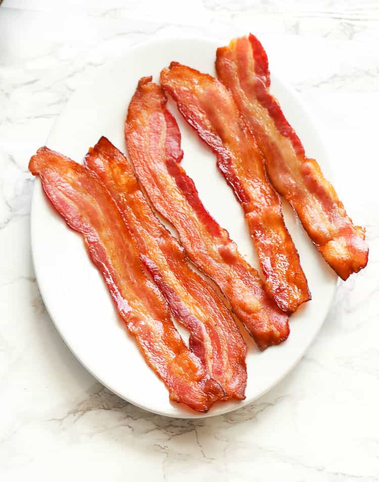 five strips of oven-baked bacon on a white oval plate