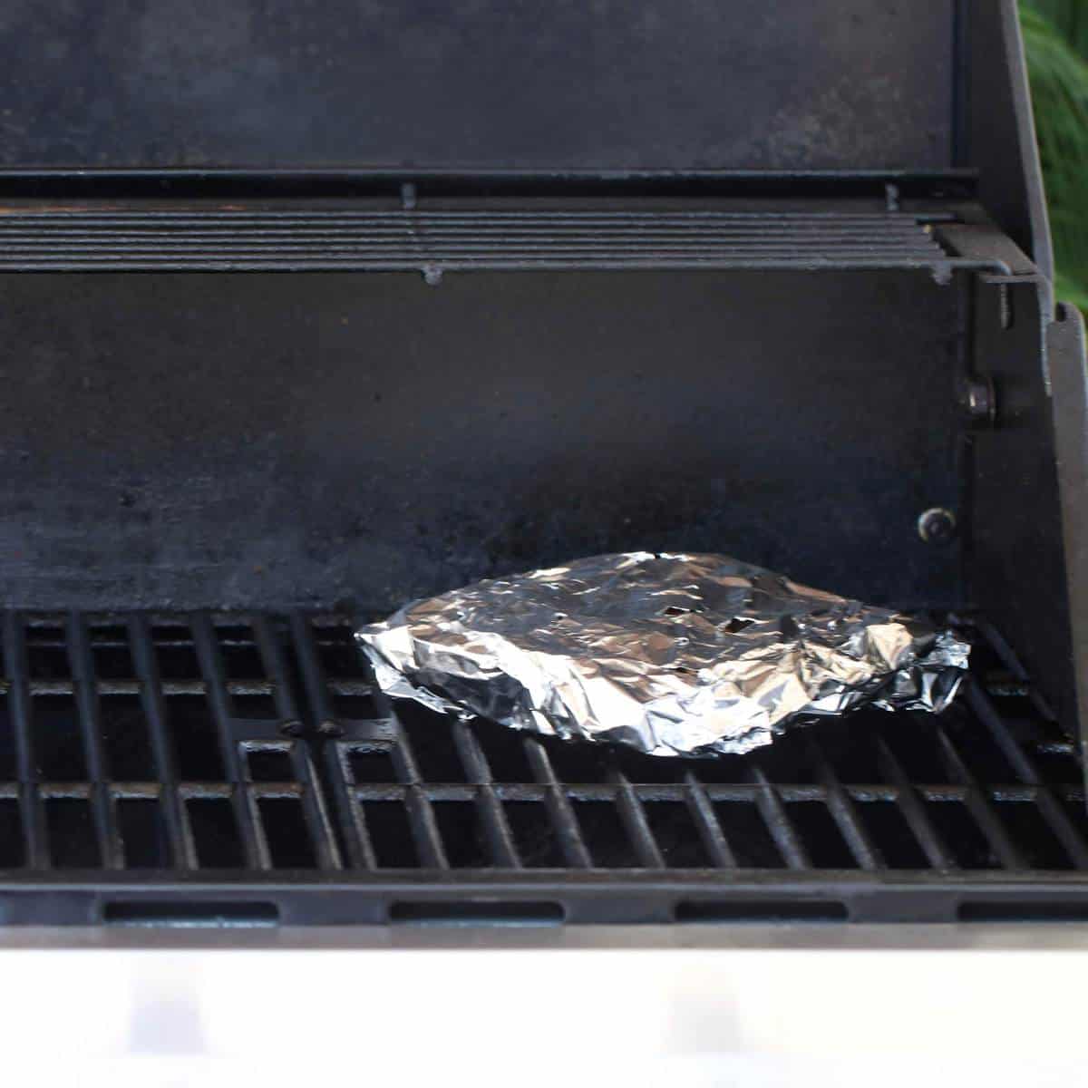 chunks of wood wrapped in a foil paper on the grill for smoking