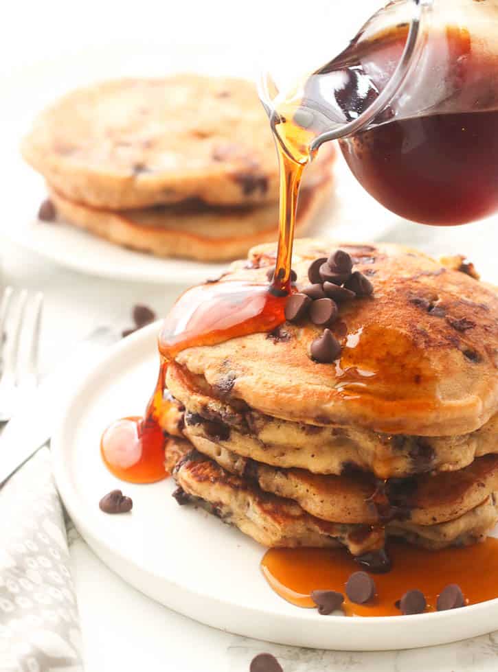 a stack of chocolate chip pancakes drizzled with syrup