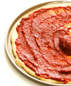 Spreading easy Homemade Pizza Sauce on a homemade pizza crust