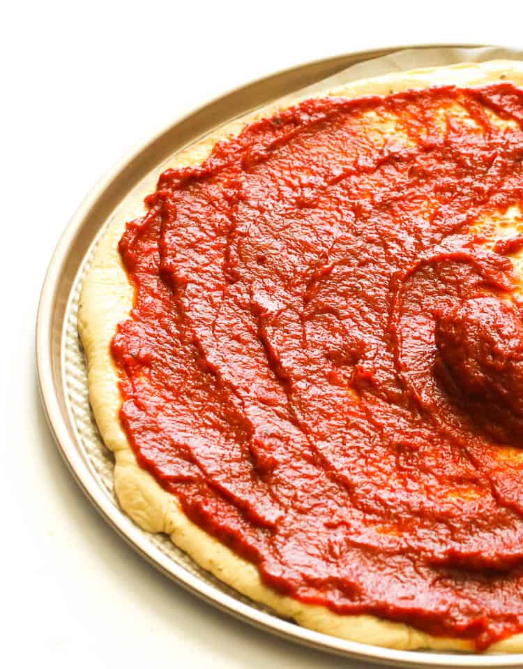 Spreading easy Homemade Pizza Sauce on a homemade pizza crust