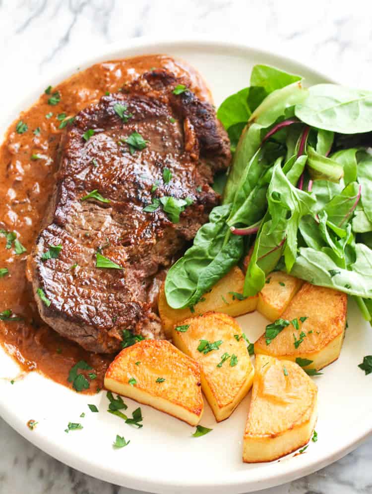 Steak Diane on plate with green salad and potatoes on the side