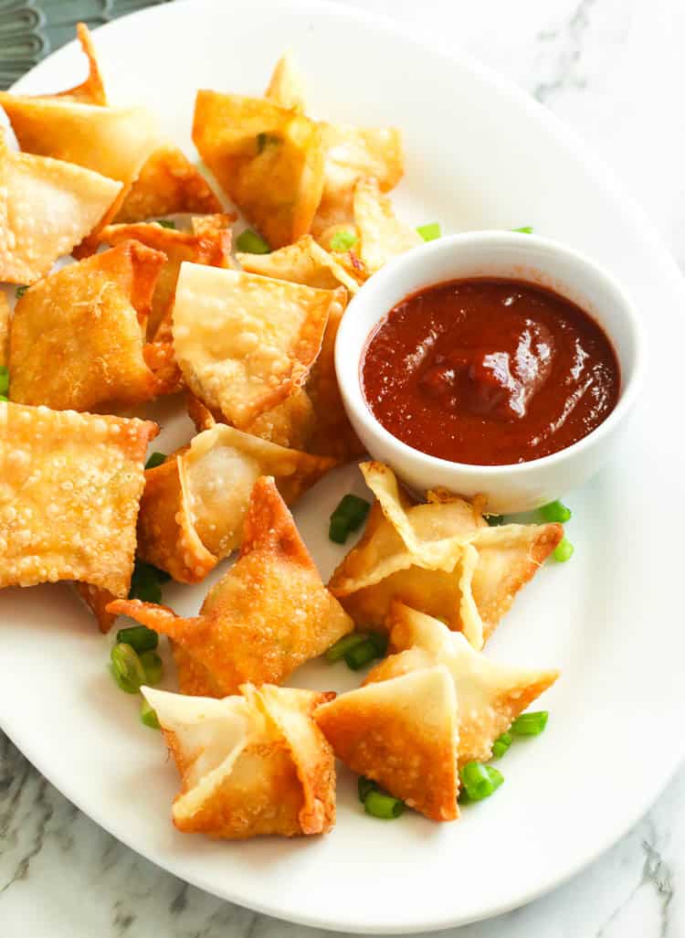 A plate full of crispy Crab Rangoon with sriracha