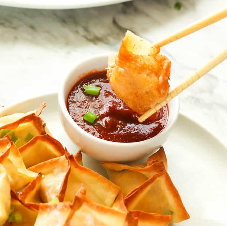 Dipping crispy Crab Rangoon in hot sauce