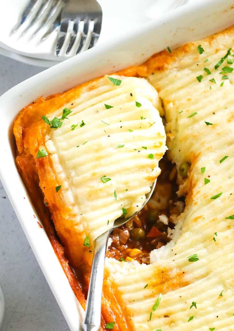 Shepherd's Pie in a white baking dish with a spoonful about to be served