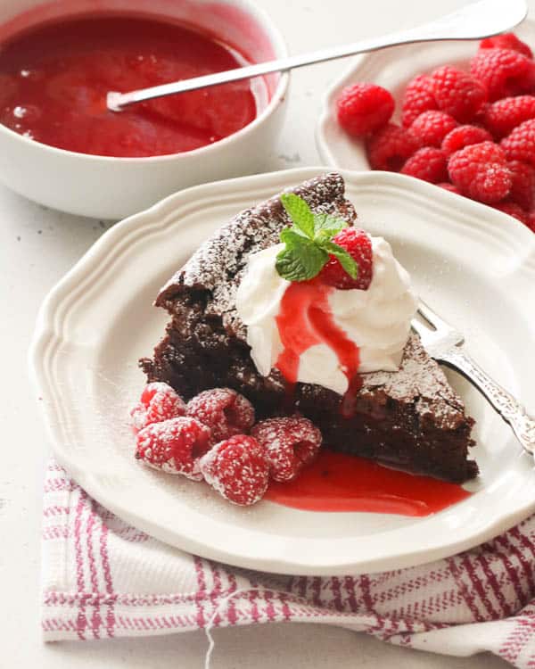 Flourless Chocolate Cake topped with homemade whipped cream and raspberry sauce