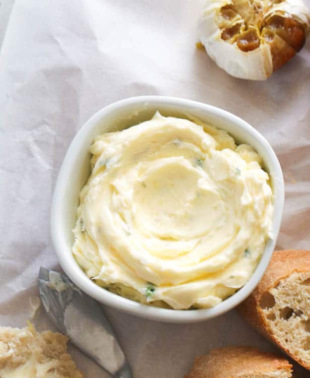 a small bowl of garlic butter with a roasted bulb of garlic and bread slices in the background