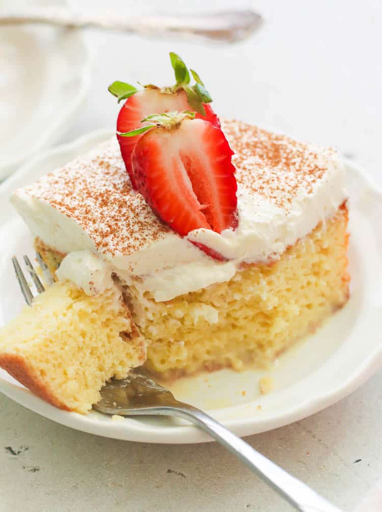 A square of tres leches cake topped with whipped cream and a strawberry. You can replace the dairy with coconut milk.