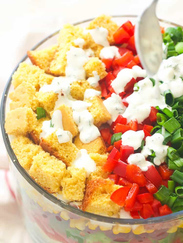 Drizzling the ranch dressing on a colorful Cornbread Salad